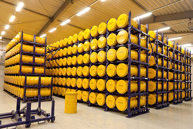 Glance into the interim storage, yellow barrels are stacked on blue metal shelves.